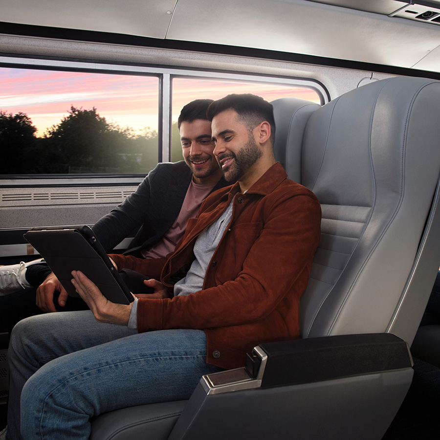 Un couple LGBTQ regarde une tablette sur leurs sièges de train.